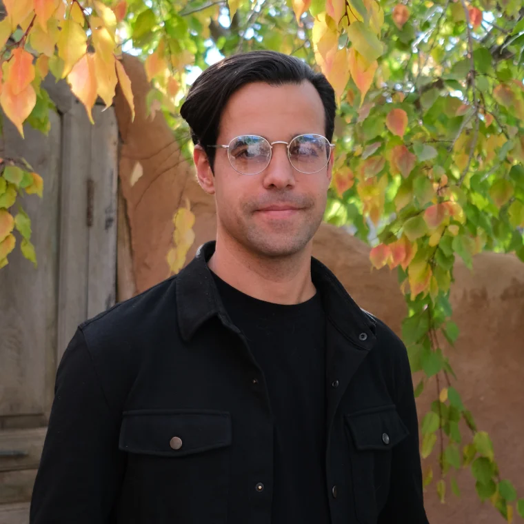 Cody Lampman, smiling, in a black jacket in front of autumn leaves